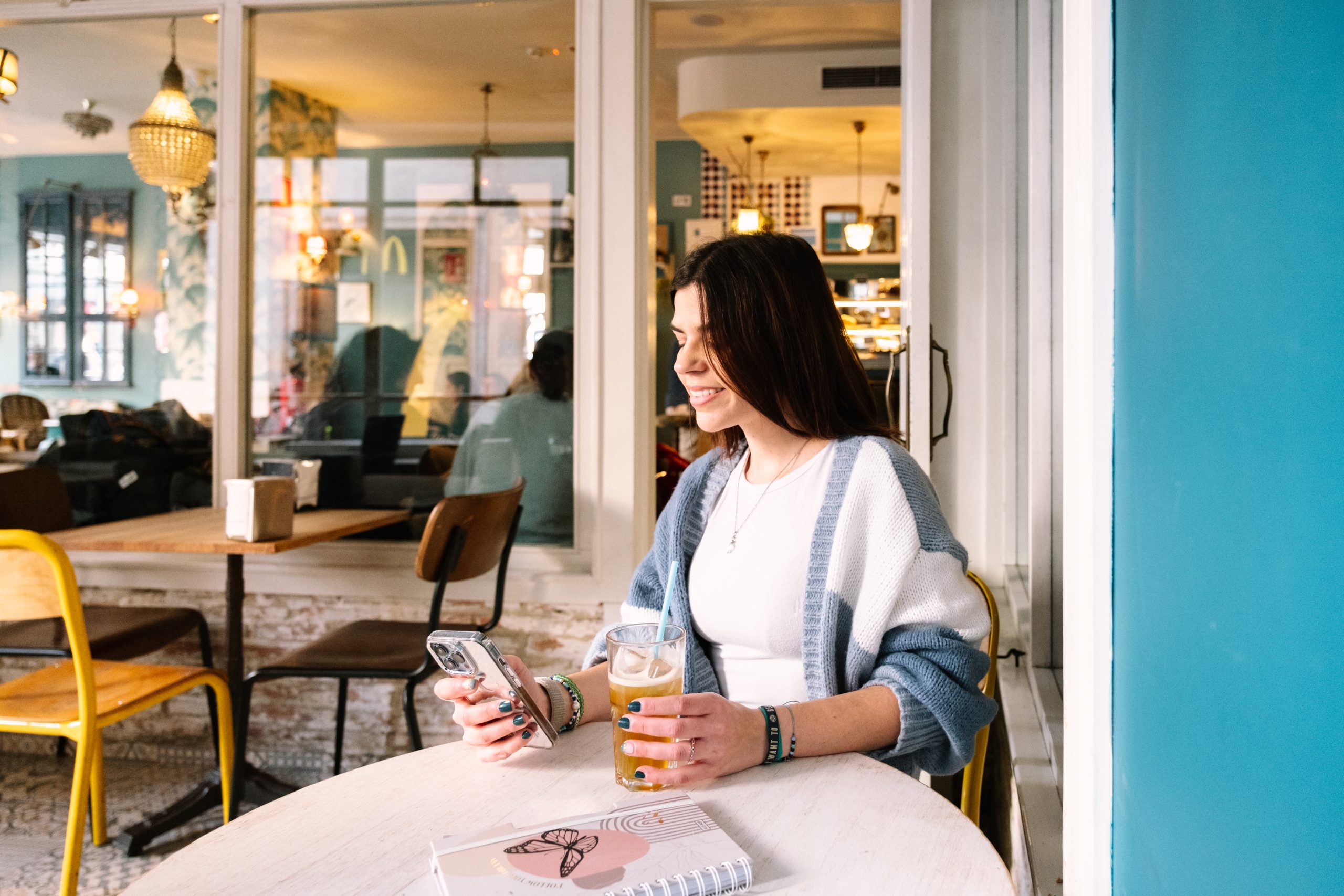 a woman sitting at a table with a drink and a phone